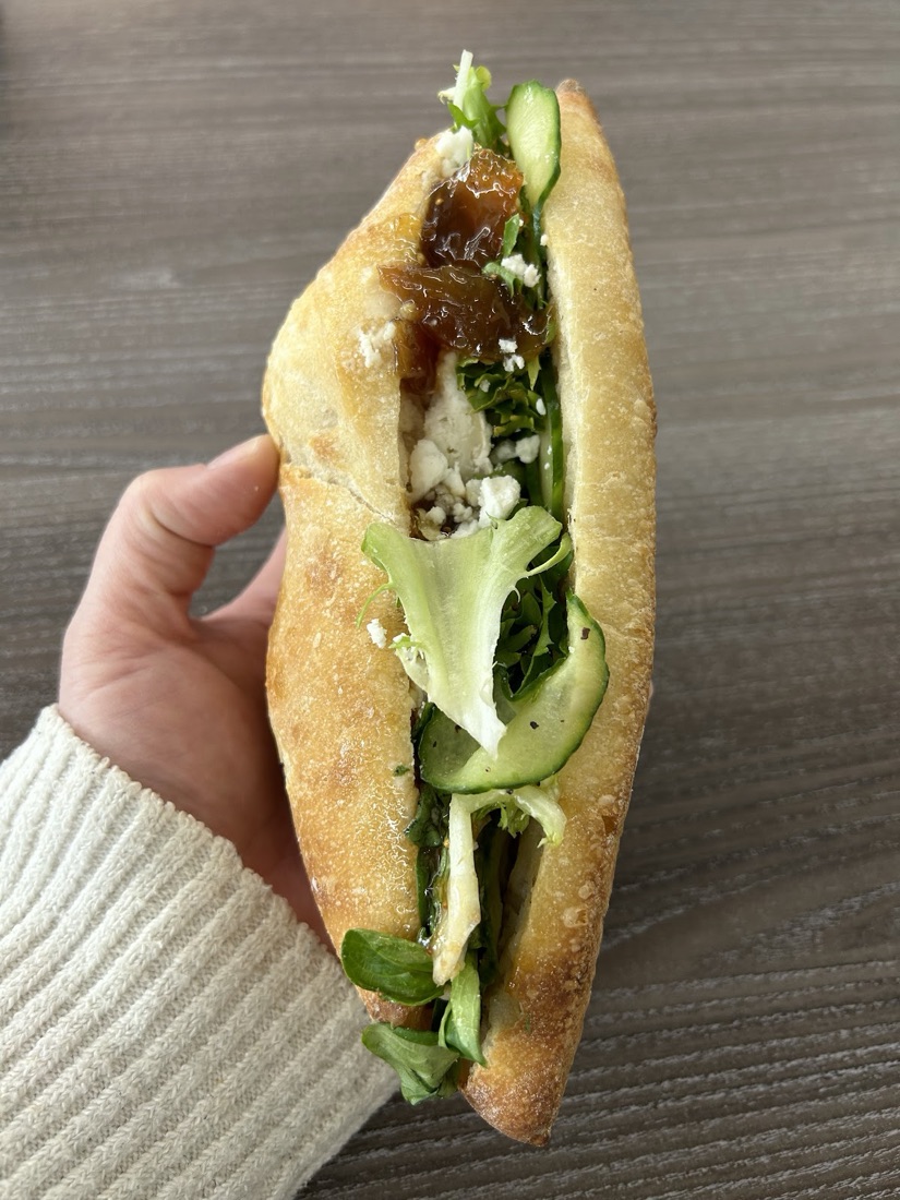 An open filled sourdough baguette with soft cheese, cucumber and fresh herbs